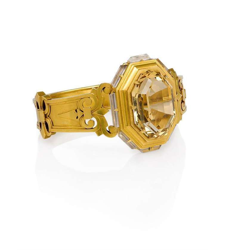 An antique gold bangle bracelet centering on an octagonally set citrine in a gold frame set with faceted crystal baguettes, with shoulders of open scrollwork design, in 18k.  Interior circumference: 6.5