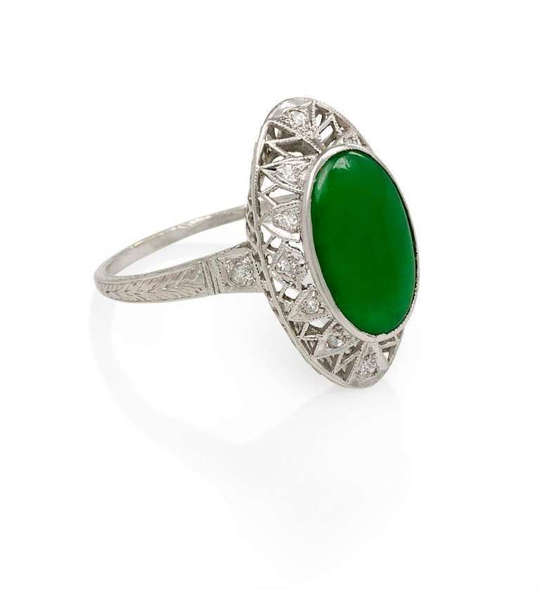 An Art Deco oval jade ring, with filigree diamond borders, in platinum.