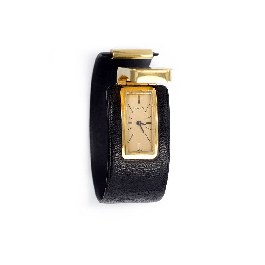 A watch bracelet comprised of a flexible black leather cuff with a rectangular covered gold face, in 18k.  Tiffany & Co.  France.  #77845.  Interior circumference: approximately 6