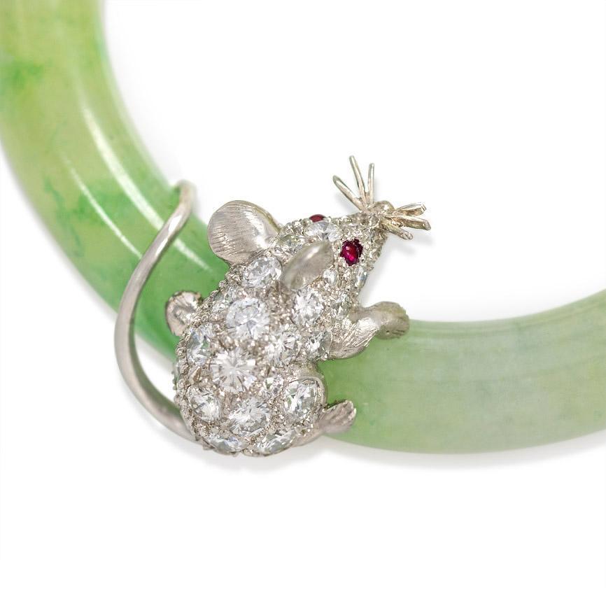 A circular blue-green jadeite brooch embellished with a diamond mouse with ruby eyes and a scrolling baguette diamond ribbon, in 18k gold and platinum.  Cartier, #6070597.
