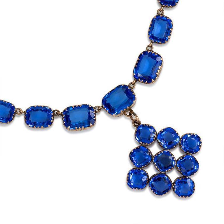 An antique blue cushion-cut paste rivière necklace suspending an openwork square cluster pendant, in 9k gold.