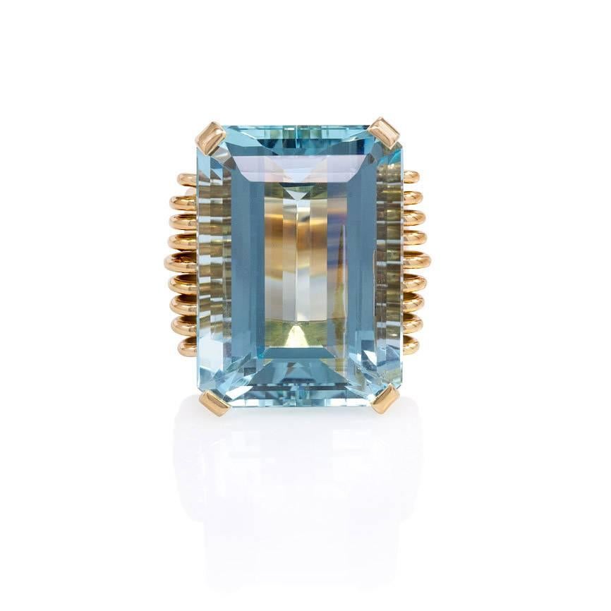 A Retro gold and aquamarine cocktail ring in a scrolled wirework mounting, in 18k.  France.  The rectangular faceted aquamarine measures 24.7 x 17.25mm; approximately 34.65 cts.