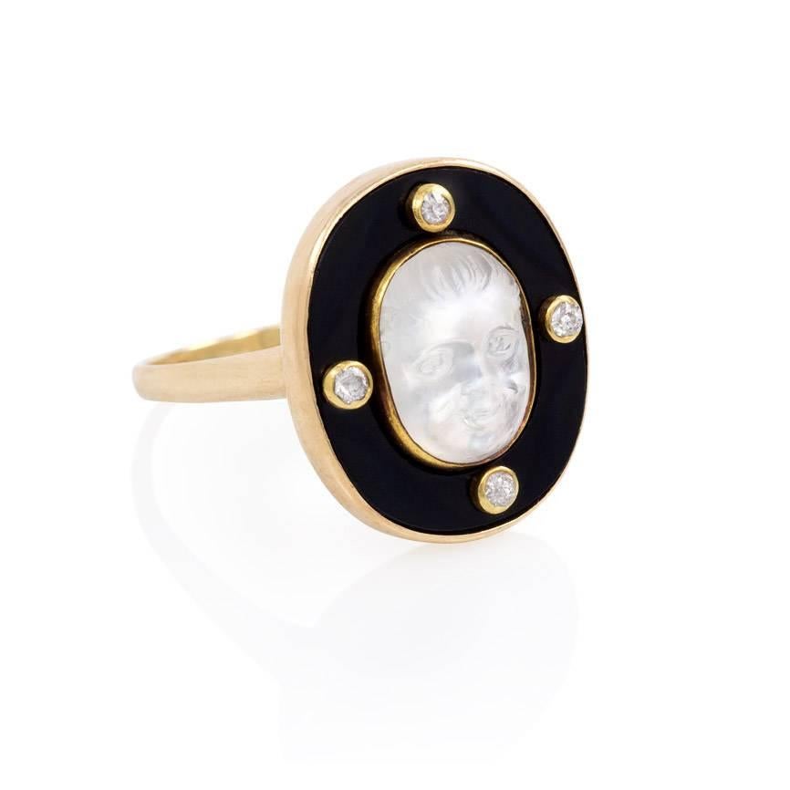 An Edwardian ring comprised of a carved moonstone cherub in an oval onyx surround with four collet-set diamonds, in 14k gold.