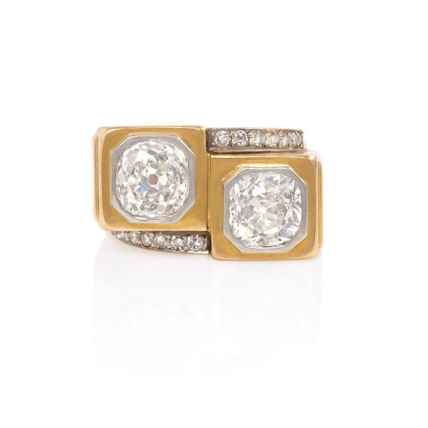 An Art Deco bypass diamond ring comprising two old mine cushion-cut diamonds in octagonal bezel settings, accented with single-cut diamonds, in 18K gold and platinum. France. Old mine diamonds weigh approx. 1.63 ct. and 1.71 ct., respectively.  Top