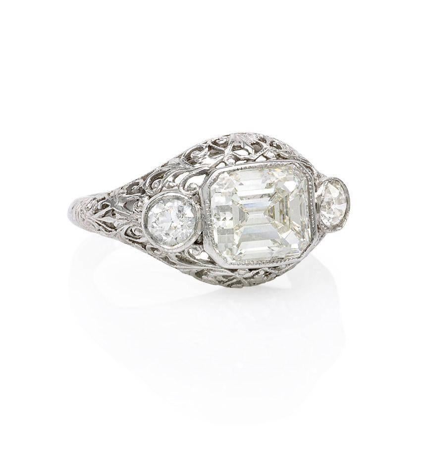 An Art Deco three-stone diamond ring, the center emerald-cut diamond of approximately 2.03 cts. flanked by two old mine cut diamonds of estimated 0.40 cts. tw, in a filigree platinum mount.  GIA report for center stone.  