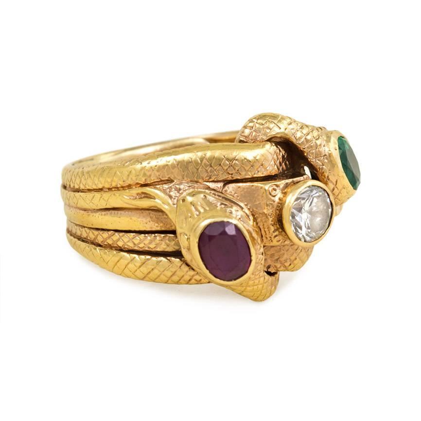 An antique gold and multi-gemstone ring with engraved detail, designed as two coiled serpents set with a ruby, diamond, and emerald, in 18K.