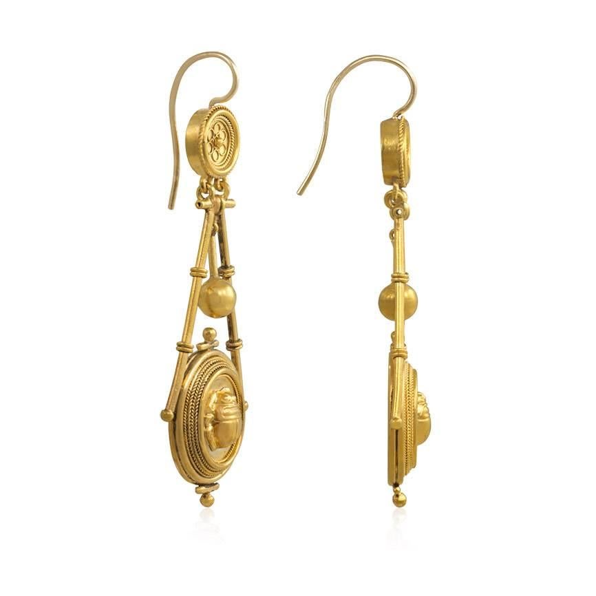 A pair of antique Etruscan revival earrings comprised of circular tops suspending oval pendants with repoussé scarabs, in 18k gold.