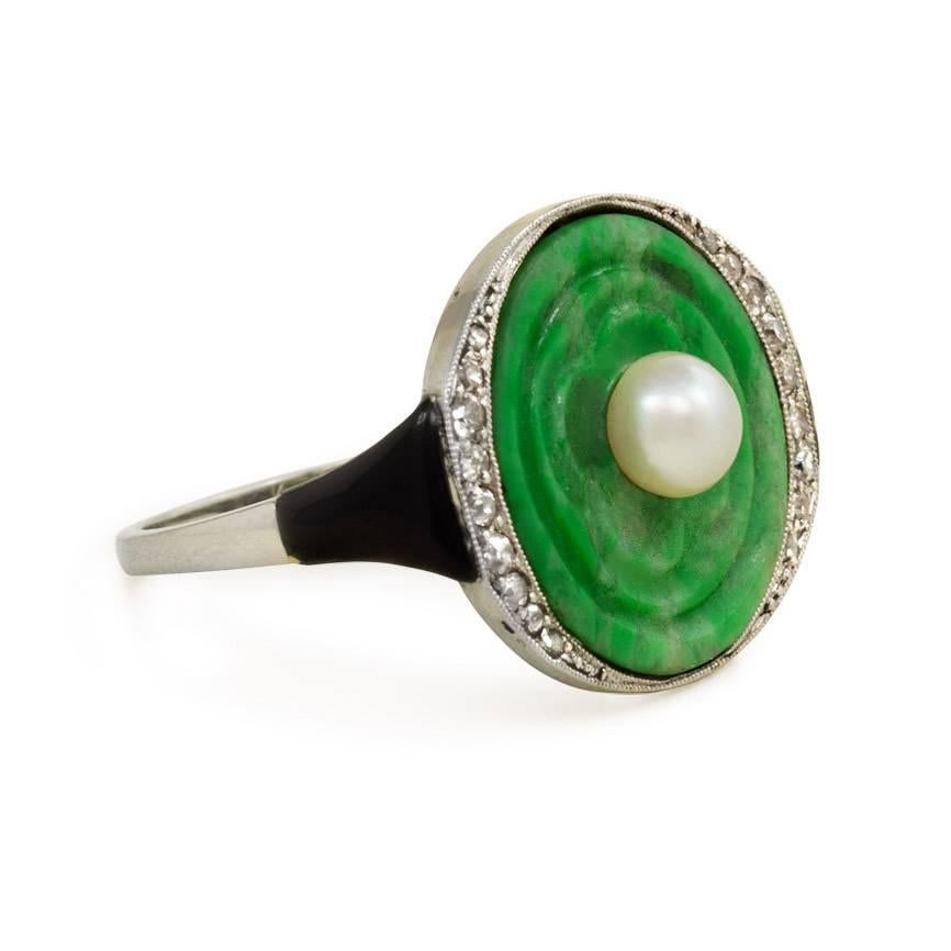 An Art Deco ring comprised of a carved jade panel set with a pearl in a diamond and black enamel mounting, in 18k white gold. Sasportas, France.

Top measures approximately 1.6 x 2cm