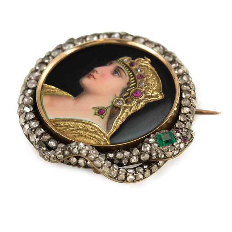 An antique enamel, diamond, and gem-set brooch depicting Cleopatra surrounded by a coiled diamond serpent with emerald-set head and cabochon ruby eyes, in silver and 18k gold. Attributed to Golay et Fils, Geneve, Switzerland