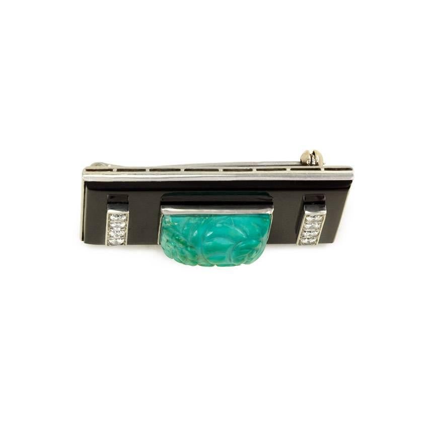 An Art Deco onyx rectangular plaque brooch featuring a carved turquoise center flanked by vertical bars set with diamonds, in platinum.