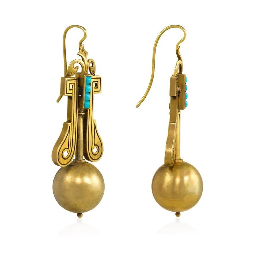 A pair of antique Victorian gold pendant earrings embellished with engraving and turquoise accents, in 15k.  The lightly textured gold spherical bead pendants are suspended from geometric and scrolled surmounts with engraved detailing, centering on