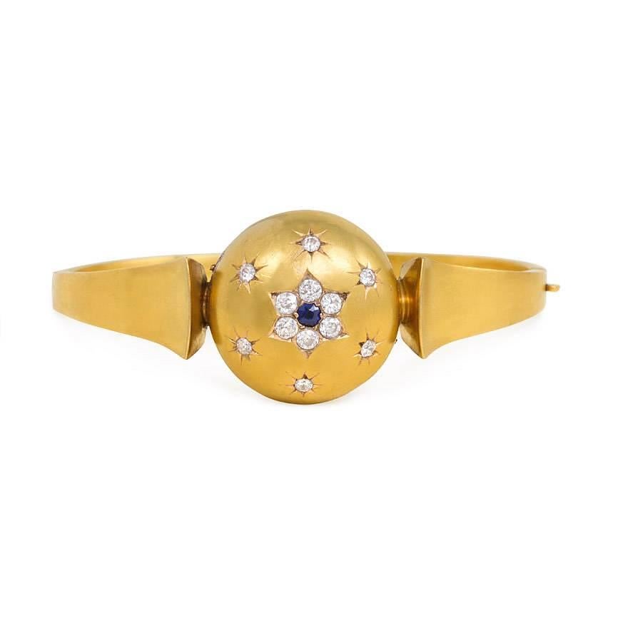 An antique gold bangle bracelet with domed center inset with a diamond and sapphire flower motif in a star-set diamond surround, with split tapering shoulders, in 15k; in antique case.  England.

Dimensions: 6 1/4" inner circumference,