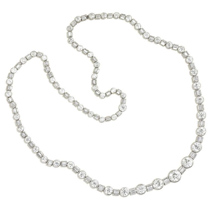An Art Deco diamond necklace, comprised of 58 collet set round European cut diamonds, separated by half cylinder links of channel set baguette cut diamonds, in platinum. The necklace contains additional clasps, and can be worn as a single 25.5 inch