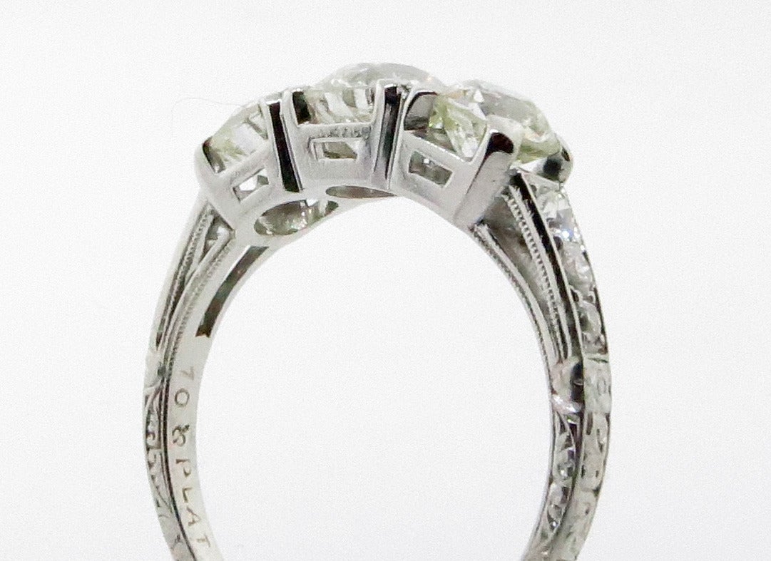 A perfect example of the classic three stone ring. The handmade engraved mount is prong set with three old European cut diamonds totaling approx. 1.65cts. grading VS clarity J color. Each side of the mount is bead set with 3 slightly graduating