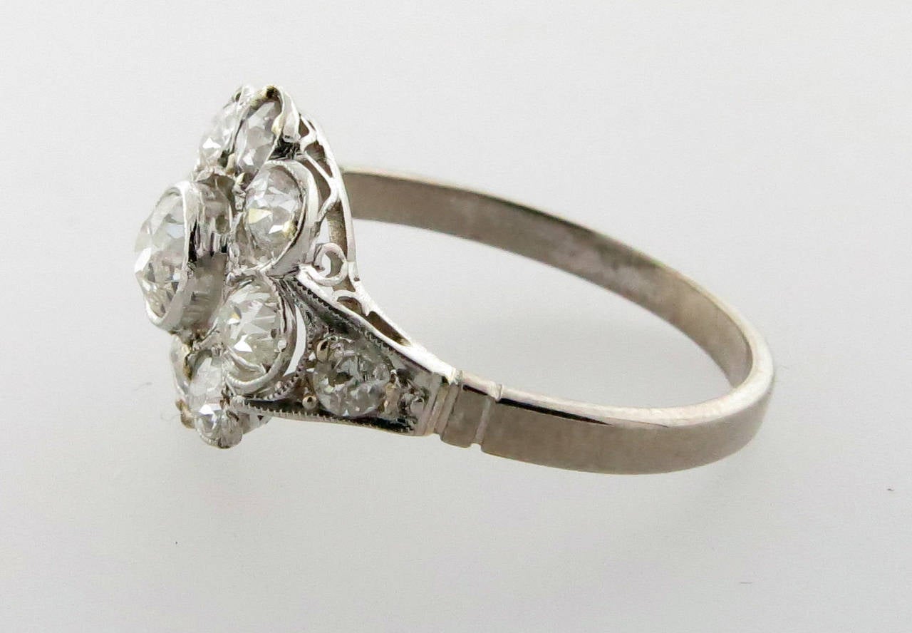 Platinum mount flower design mount ring circa 1920. The center is bezel set with an old mine cut diamond weighing approx .25cts. surrounded by eight bead set diamonds with a diamond accent on each side of the shank totaling an additional .50cts. The