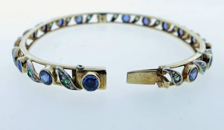 Charming 14kt. yellow gold hinged bangle bracelet bezel set with 18 round old faceted natural cornflower blue sapphires totaling approx. 4.5cts. alternating in platinum with 18 cushion and round faceted natural emeralds totaling approx .50cts. The