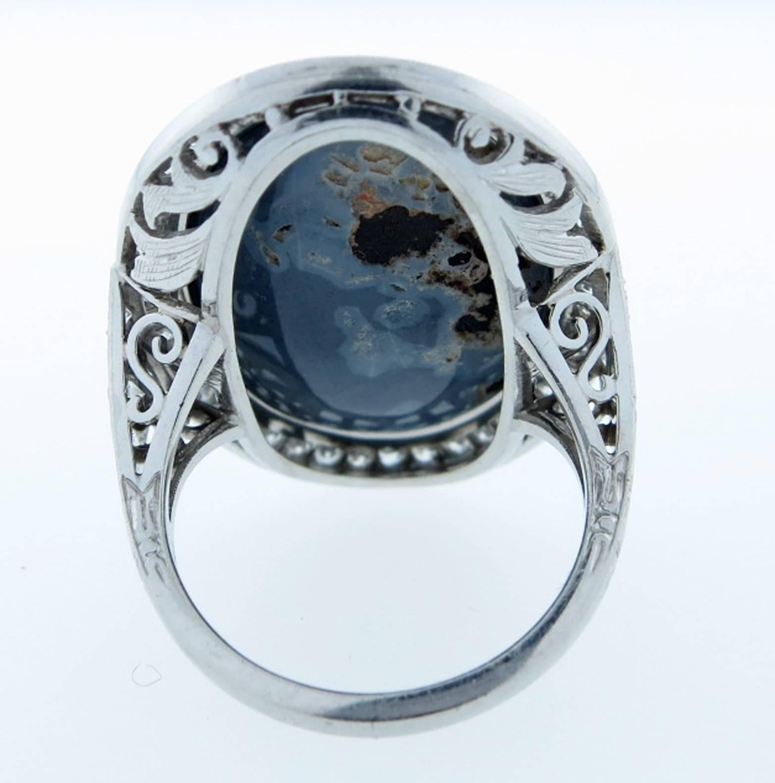 Handmade platinum mount bezel set black opal center measuring approx 23. mm. x 15.5mm. x 5.0mm. weighing approx 9 1/2 cts. surrounded by 44 bead set round old cut diamonds totaling approx .50cts. The open work engraved mount is bead set with 3 round