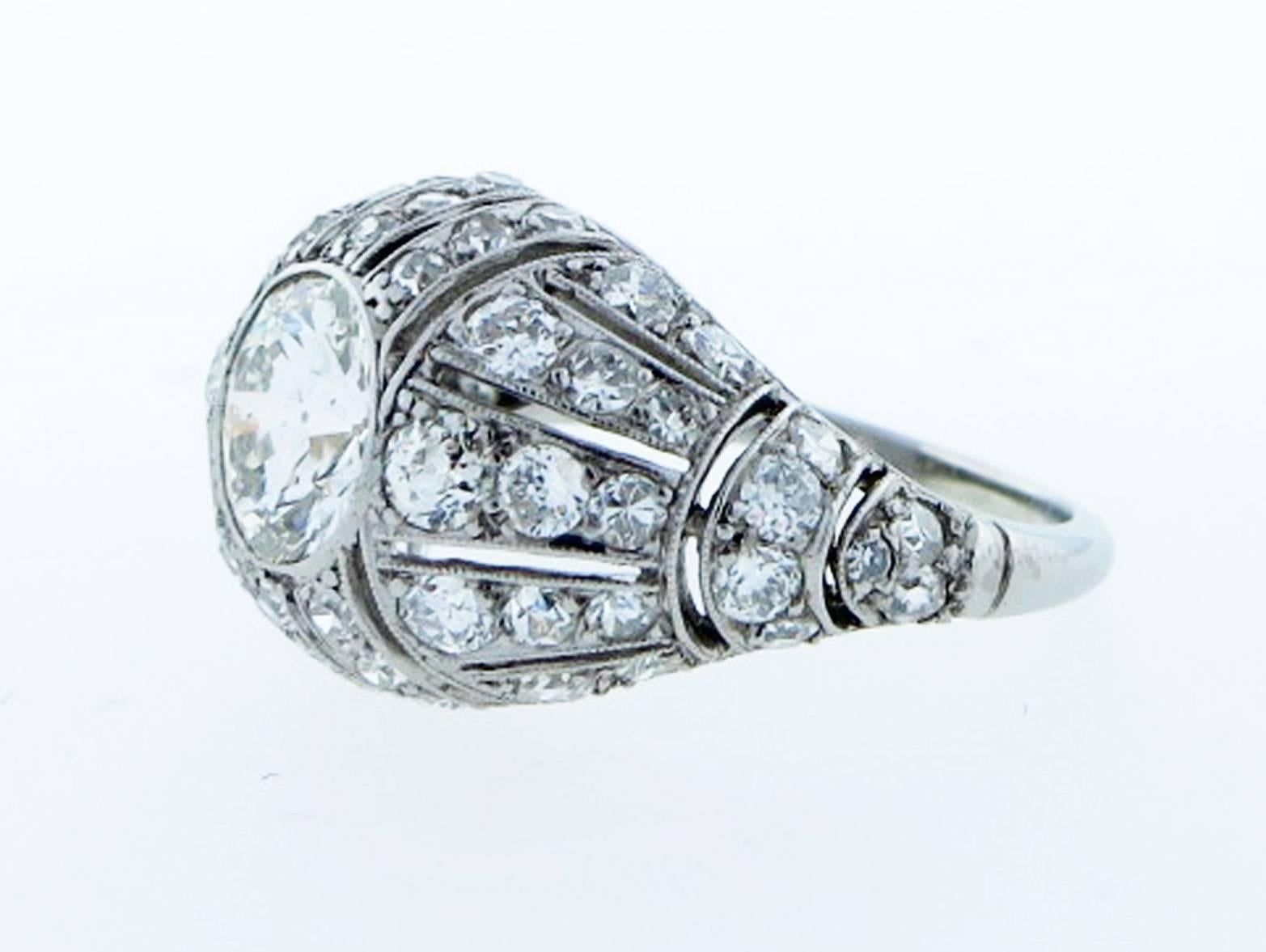 Platinum open work period 1930's Art Deco ring bezel set with a center round European cut diamond  weighing approx 1.3 cts. grading J color SI clarity. The pierced wrap around dome mount is bead set with 57 round European cut diamonds totaling