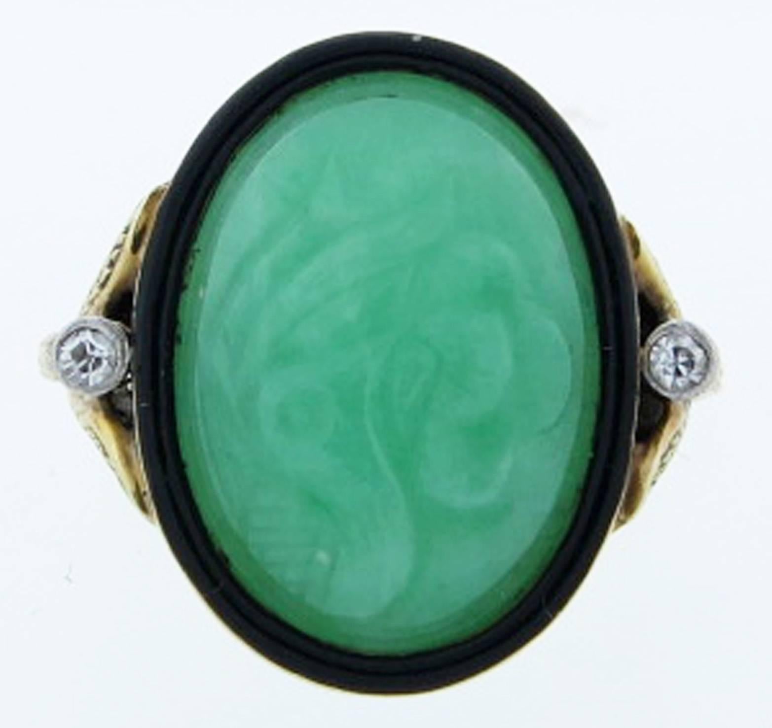 Intricate 14kt. yellow gold mount ring with an oval carved floral design jade center edged in black enamel. Each side is bezel set in white gold with a round old cut diamond. Size 6 1/2 and can be sized circa 1920.