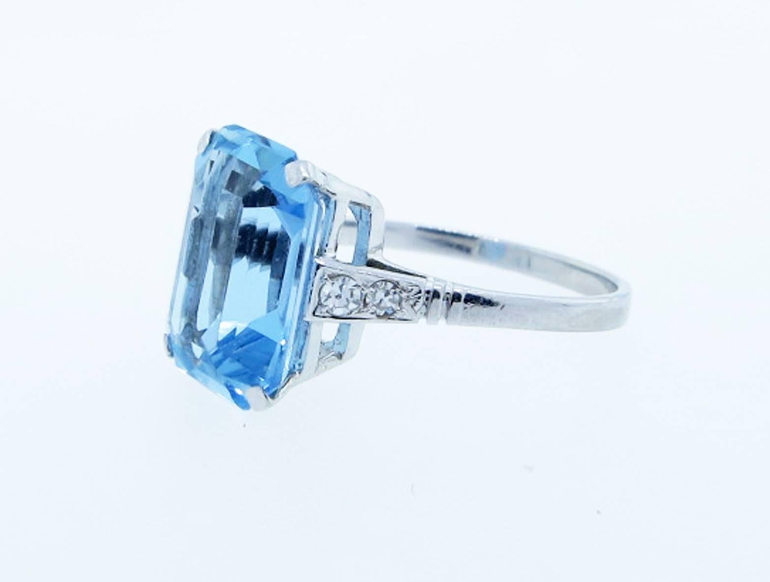 Simple platinum mount aquamarine ring prong set with a faceted emerald cut center natural sky blue aquamarine measuring 12.6 mm. x 9.3mm. weighing approx 3.75cts. Each shoulder is bead set with two round diamonds totaling approx .10 cts.Size 6 and