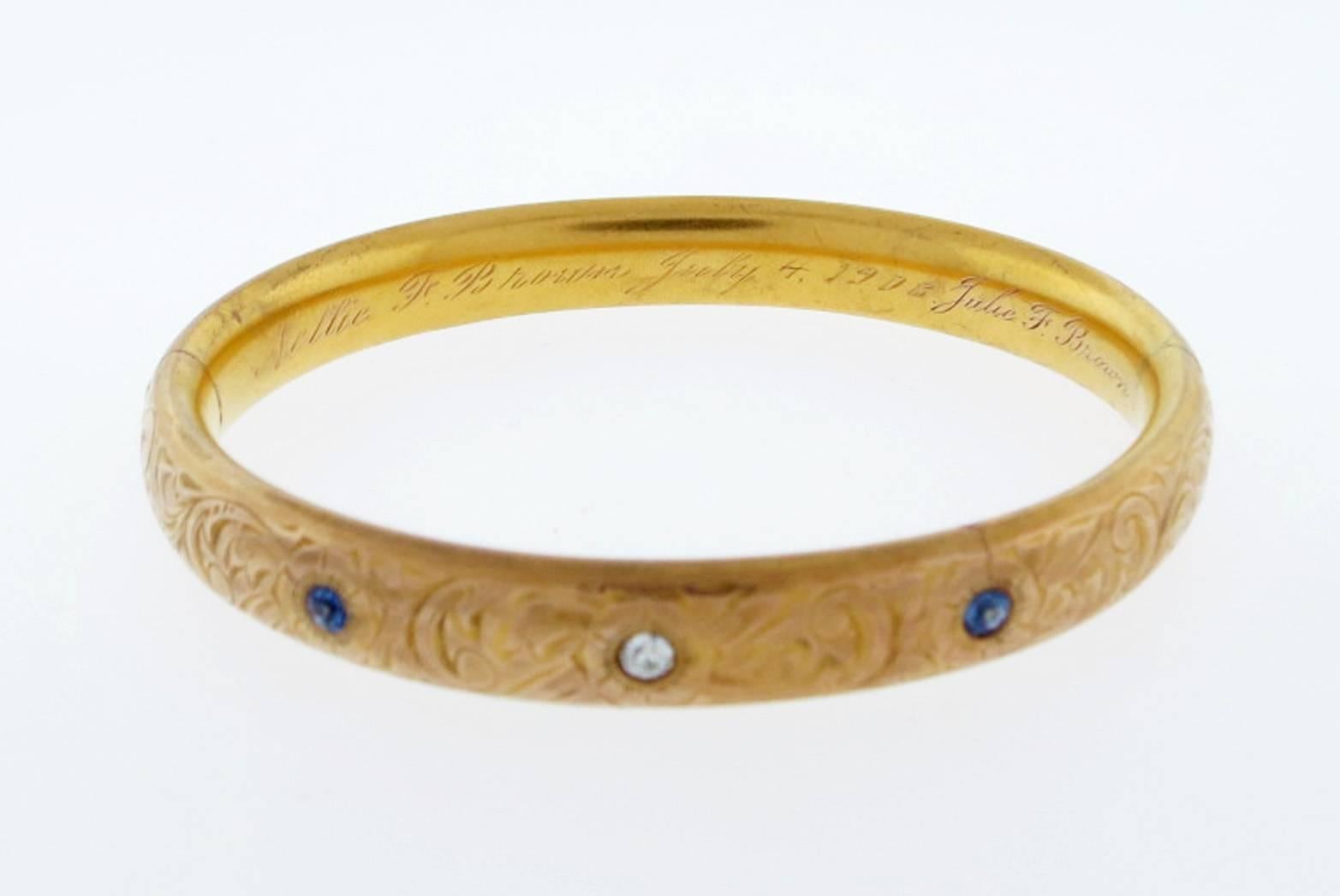 Exceptional condition 14kt. yellow gold engraved hinged bangle bracelet with sapphires and diamond. The center is bead set with a round European cut diamond weighing approx .15cts. set on each side with a natural cornflower blue sapphire totaling
