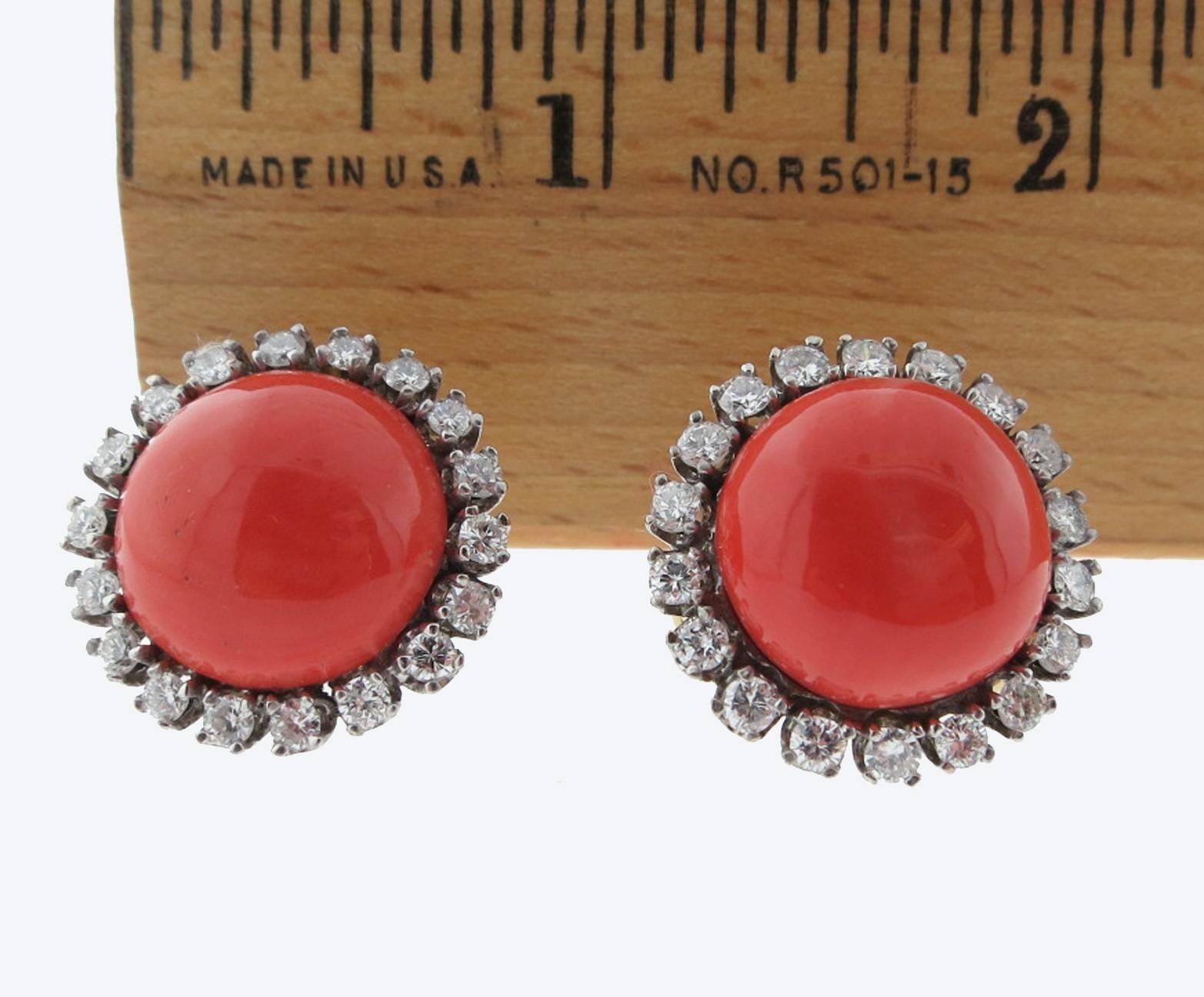 Classic natural coral button earrings surrounded with diamonds. Each earring measures approx .75 inches and is set with a coral cabochon measures approx 12.5mm. surrounded with 18 round brilliant cut diamonds in platinum. Total diamond weight approx