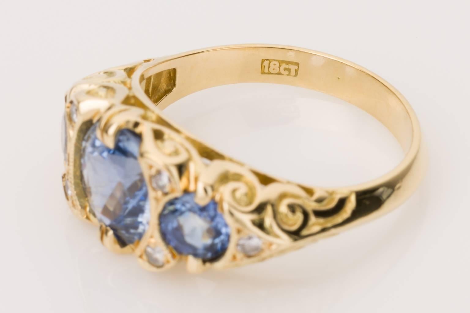 Do you love sapphires that have the most superb blue & lilac tones? Then this ring is for you. An 18k yellow gold London Bridge style ring with detailed filigree sides, containing three claw set Ceylon sapphires and six grain set diamonds mounted