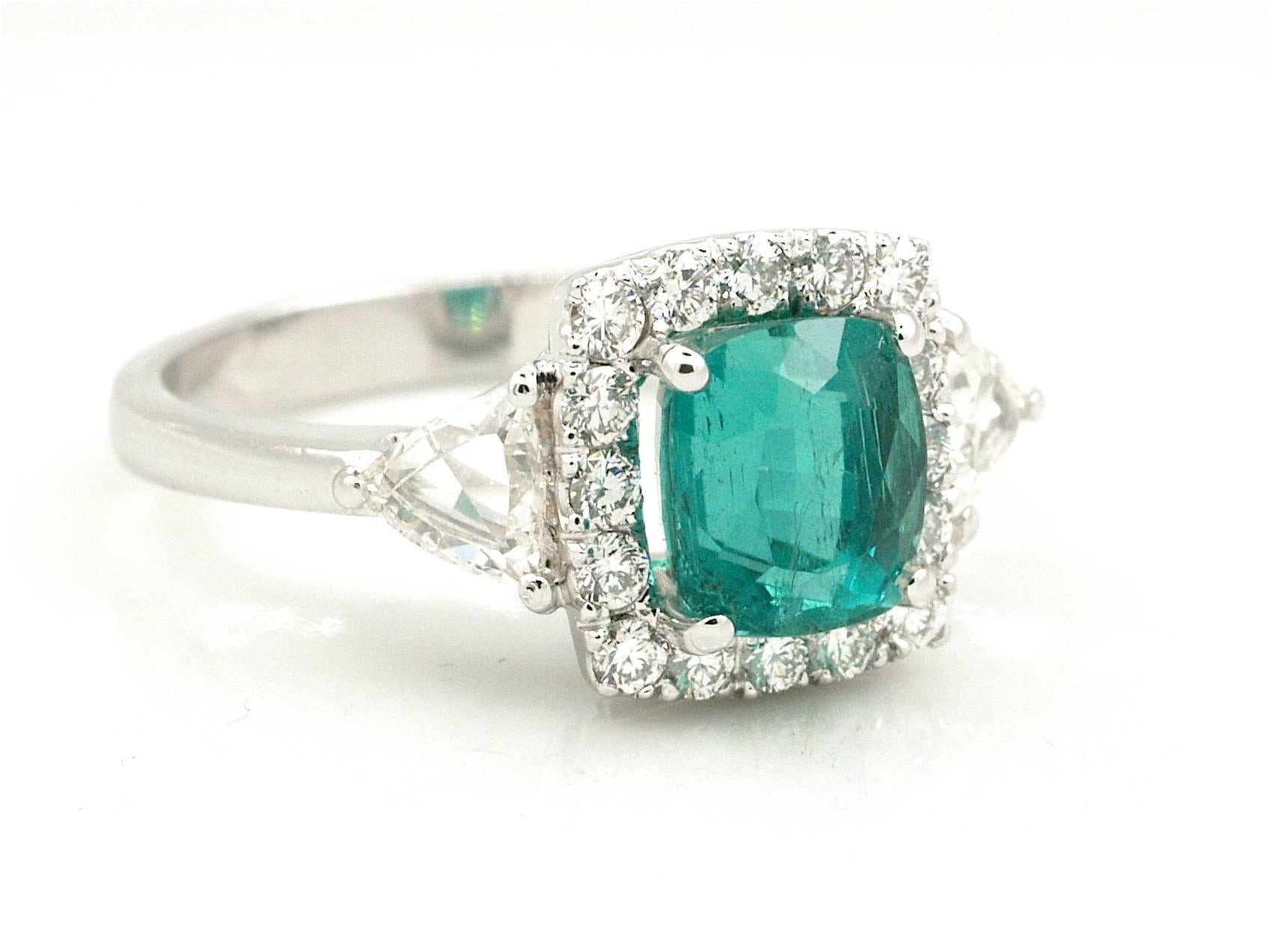 This gorgeous ring is centered with 1 genuine cushion cut emerald weighting 1.77ct, prong set,  It is flanked by a row air of brilliants cut diamonds and 2 trillion cut diamonds cumulatively weighing 0.82 cts, graded G-H color and VS clarity. This