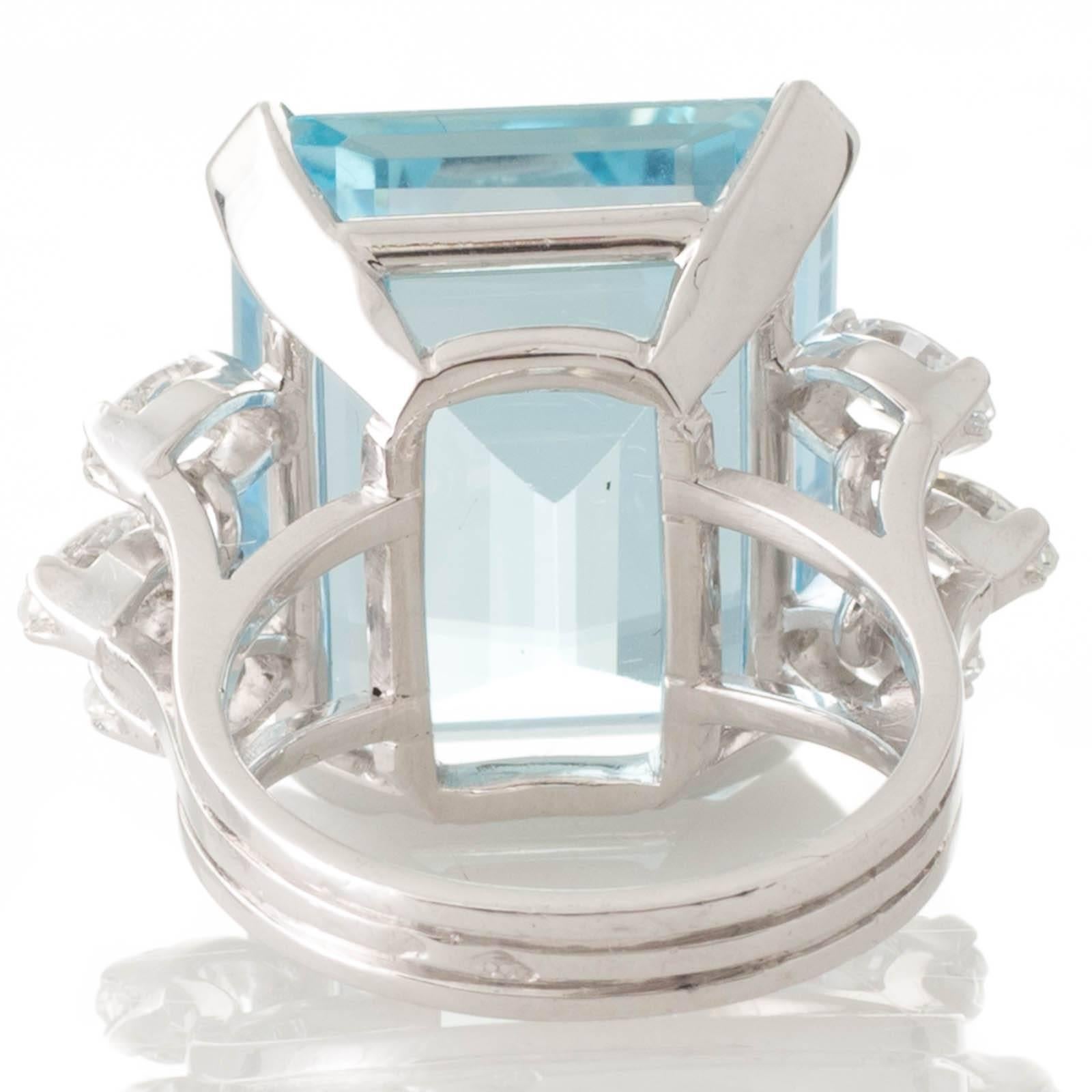 An 18ct white gold ring with an emerald cut aquamarine of estimated weight 28.18ct to the centre in four claws and three marquise cut diamonds to either side above a split and cut out underrail to the band which is formed by three fused individual
