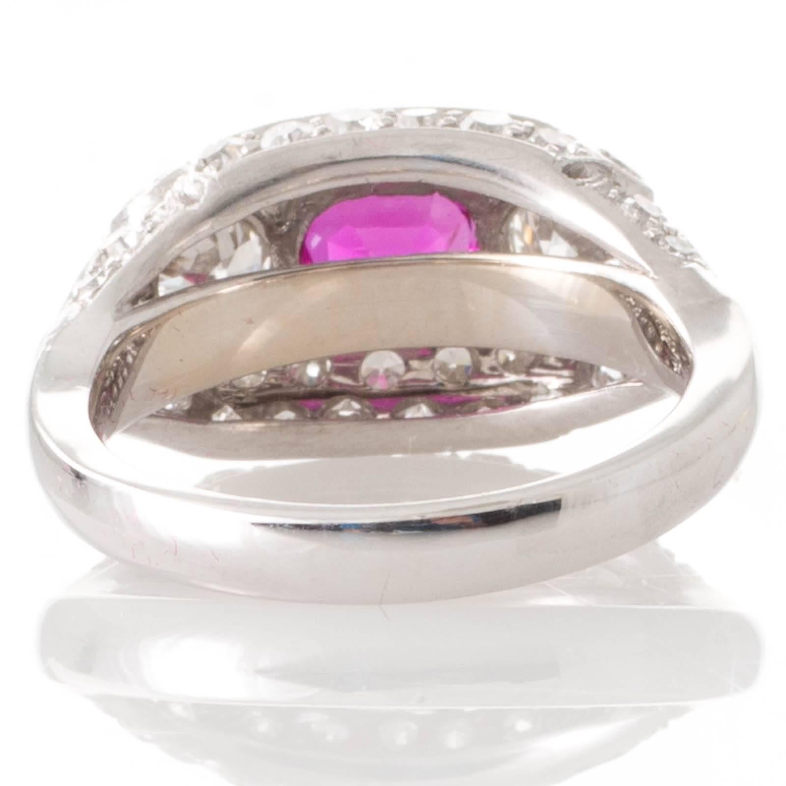 An Art Deco ring featuring an oval faceted AGL certified unheated Burmese ruby of estimated weight 0.94ct set to the top of the raised and rounded platinum mount and flanked to either side by a transition cut diamond in a floating setting grain set