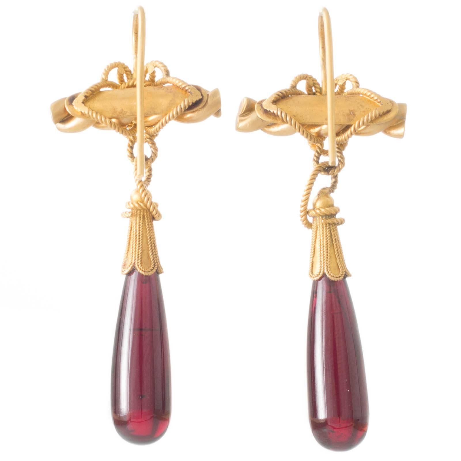 Antique earrings in yellow gold (testing as 20ct) each with decorative woven gold wire work around a horizontal twisted bar of gold connecting to polished garnet drops held in fluted gold tops all to fixed shepherd hooks. Weight: 12.9grams. 