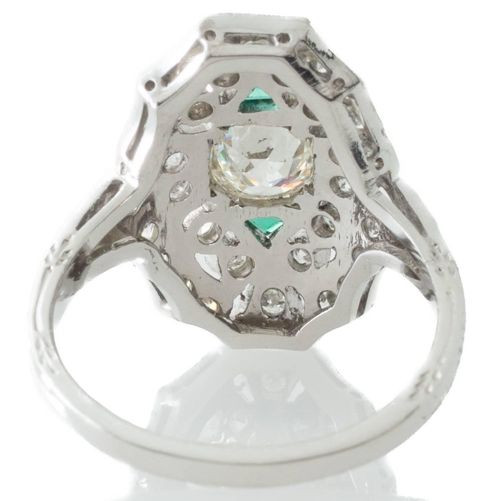 A platinum Art Deco ring with a domed plaque set to the centre in an octagonal millegrained edge setting with a 0.45ct transition cut diamond highlighted at the north and south ends with a triangular cut emerald to a surround of grain and bezel set
