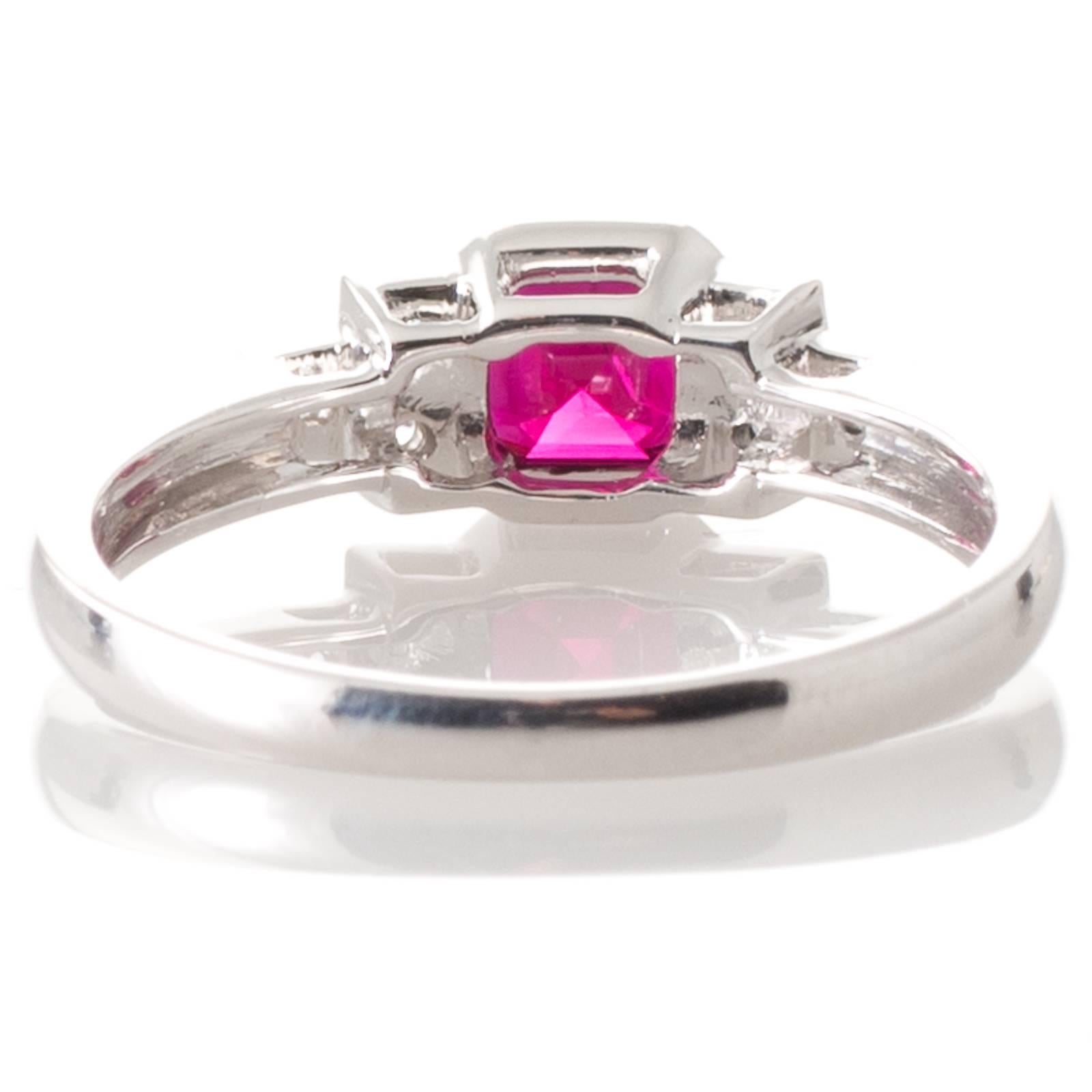 An 18ct white gold ring set to the centre in a millgrained bezel with a 0.76ct square emerald cut ruby and in stepped down shoulders to either side a pair and then a single round brilliant cut diamond to a plain polished band. Total Ruby Weight: