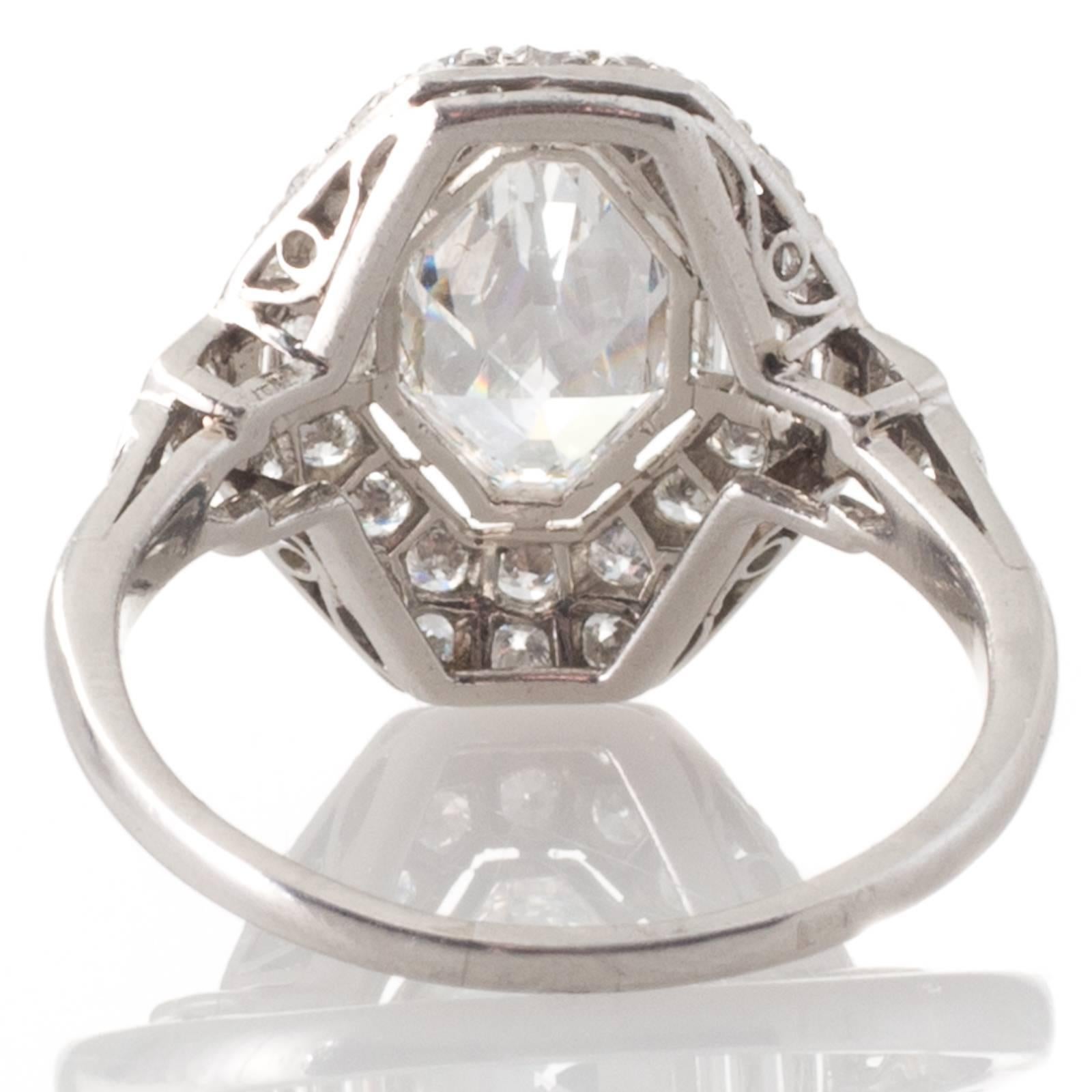 A French platinum plaque ring featuring a bezel set modified baroness cut diamond of estimated weight 1.00ct graded colour H-I clarity VS1 surrounded by thirty two grain set early modern brilliant cut diamonds and six channel set baguette cut