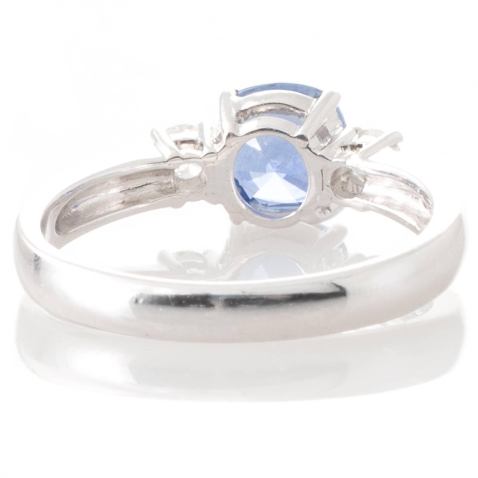 An 18ct white gold ring featuring a cushion cut sapphire weighing 1.31ct, four claw set between two round brilliant cut diamonds also claw set to upswept shoulders and a plain polished band. Total Sapphire Weight: 1.31ct Total Diamond Weight: 0.24ct