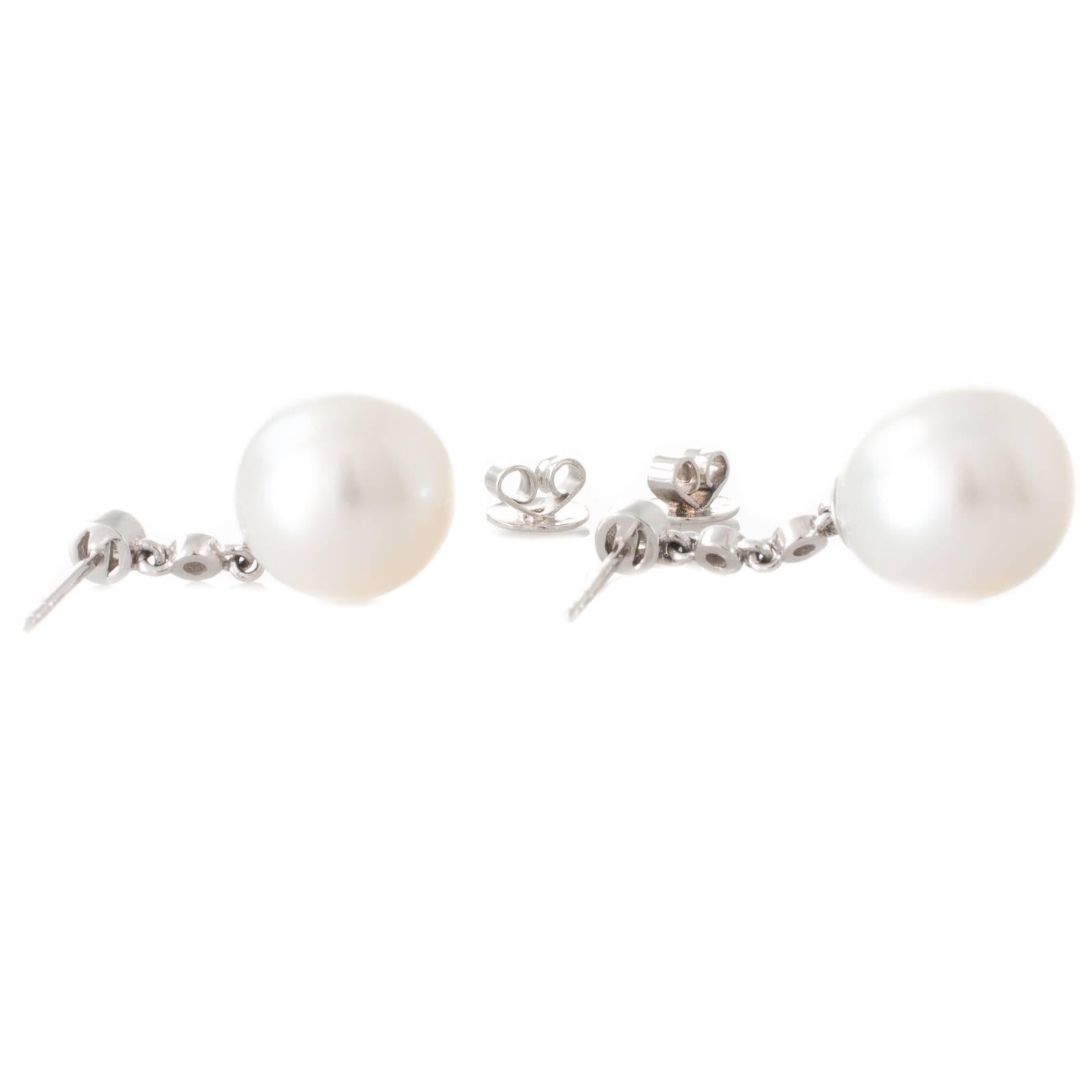 A pair of drop shaped Australian white South Sea pearl and bezel diamond drop earrings in 9ct white gold with pearls measuring 11.5 - 13.5mm with a good lustre and few natural surface marks.  
Total Diamond Weight: 0.36ct