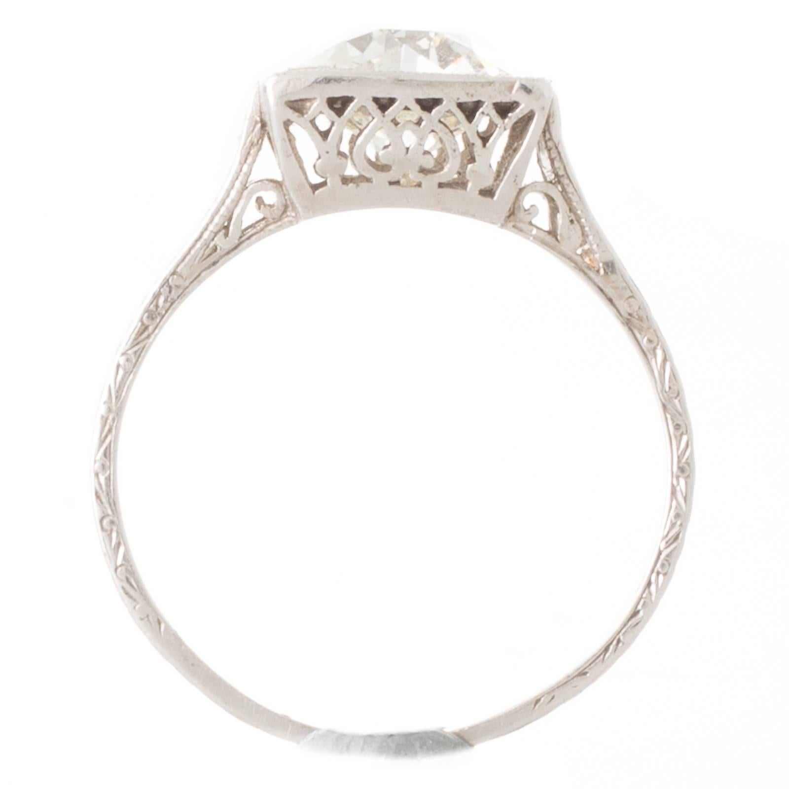 A platinum Art Deco ring featuring a 1.46ct old cut diamond, graded as colour K clarity VS1, grain set to a millegrain-edged square box mount with fine pierced detail through the gallery, all between engraved high upswept shoulders that taper down