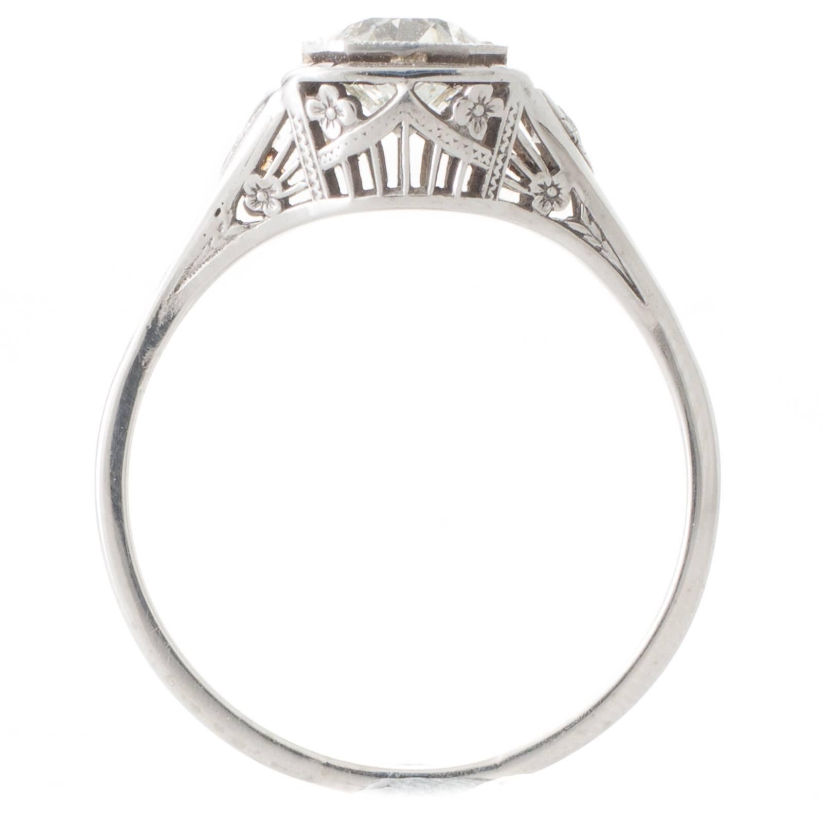 An 18ct white gold Art Deco solitaire ring featuring a 1.02ct old cut diamond, graded as colour I-J clarity VS1, bezel set within a mille grain edged spaced square plaque all above a detailed pierced and engraved gallery, the pierced tapering