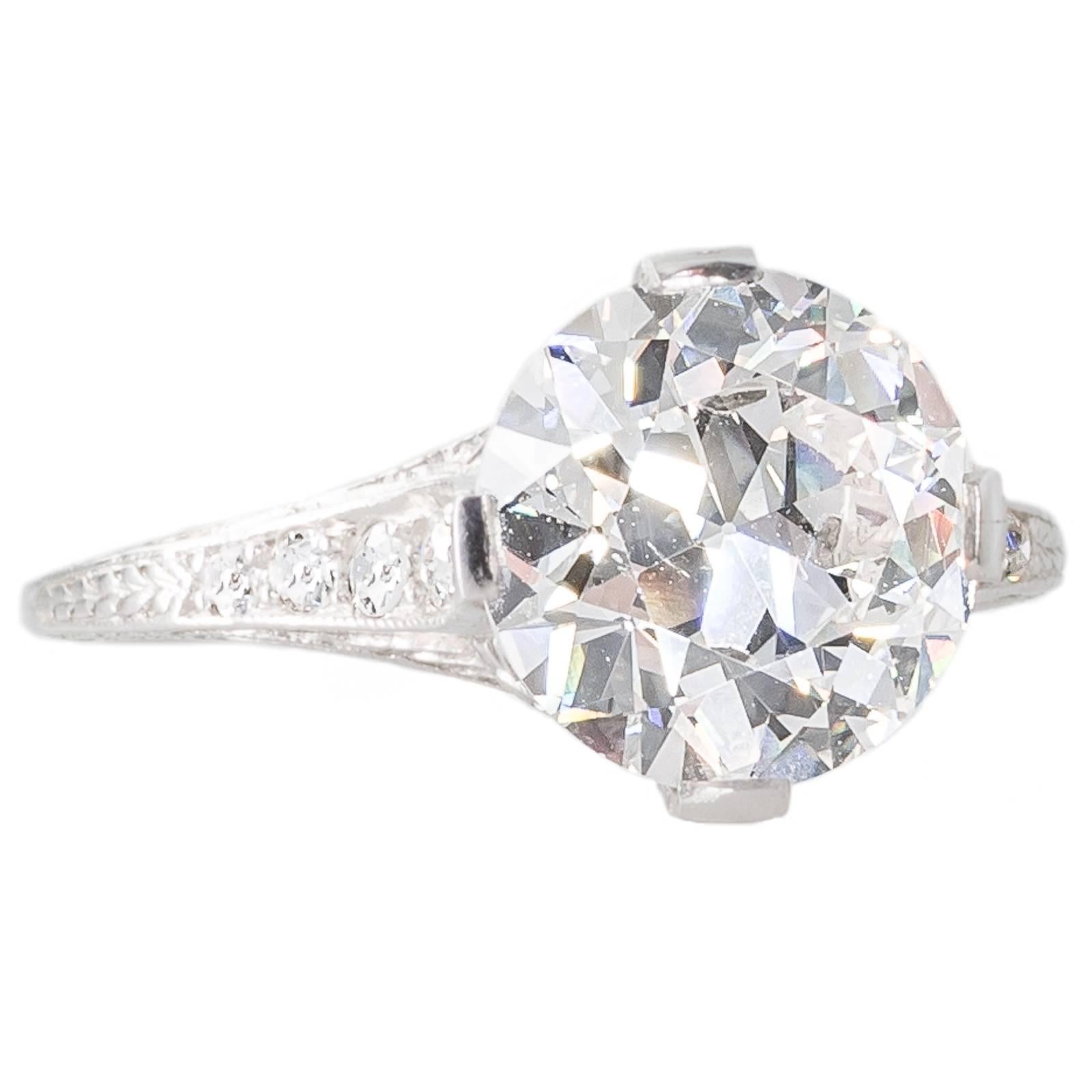 An antique platinum solitaire ring, featuring a 3.11ct transition cut diamond, graded as colour G, clarity SI1, accompanied by a GIA certificate, set in four engraved claws that follow down the finely pierced linear gallery which flares out at