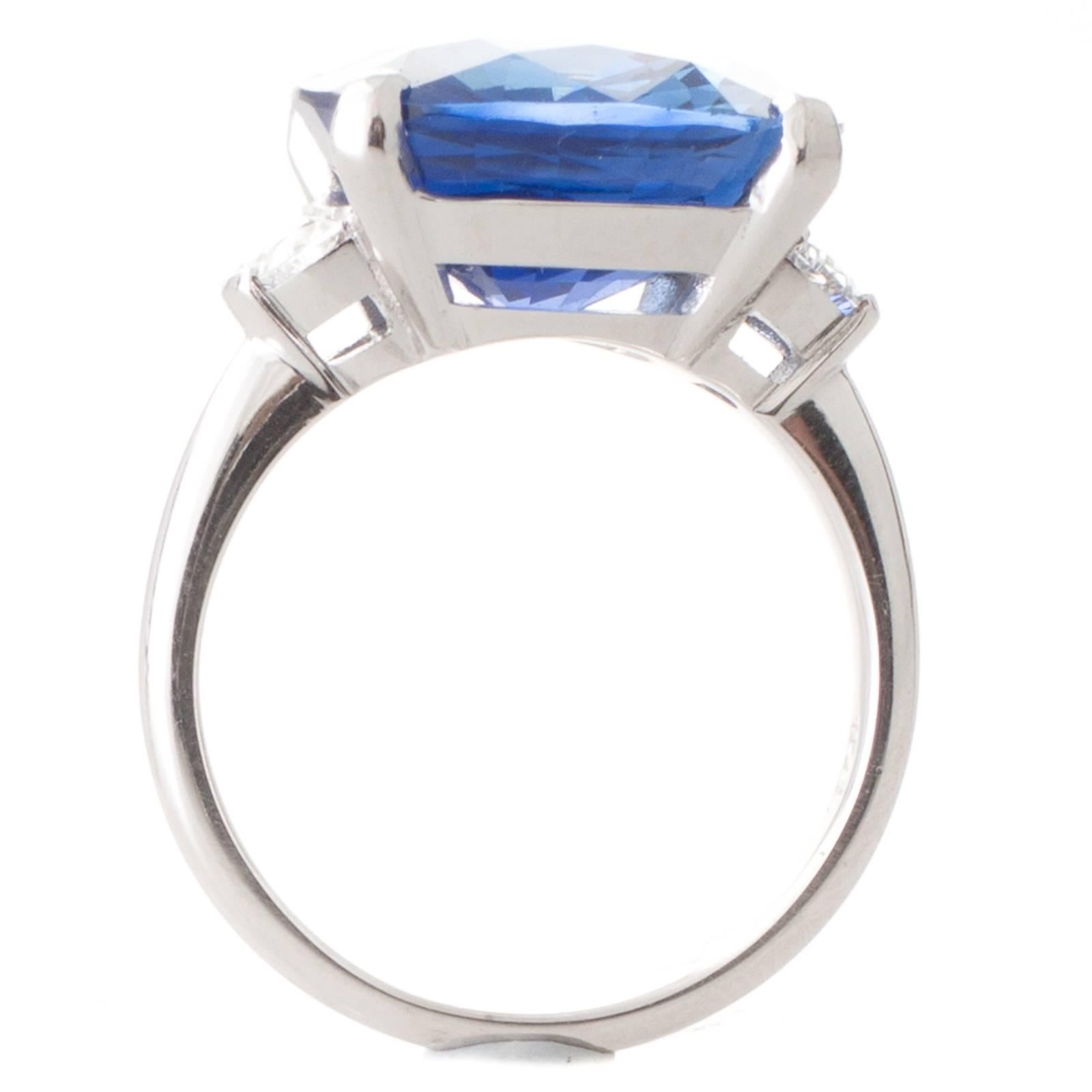 A handmade 18ct white gold ring, featuring a 12.01ct cushion cut sapphire accompanied by a GRS certificate stating origin as Sri Lankan, set in four claws between a pair of half moon cut diamonds totalling 0.36ct of colour G-H, clarity SI, all to a