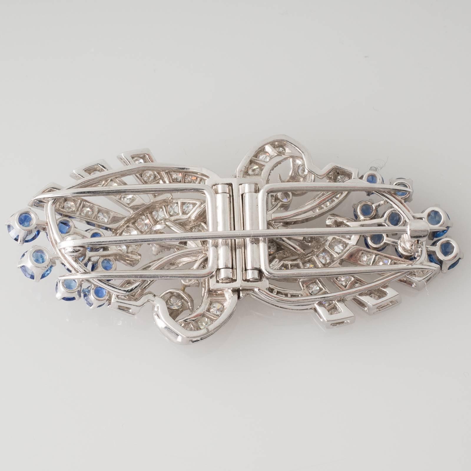 A pair of platinum dress clips each clip set with round brilliant cut diamonds on a stylised scroll and fan motif and set with eight round blue sapphires each clip with two pins to the rear both clips attach to an open frame to form a brooch the