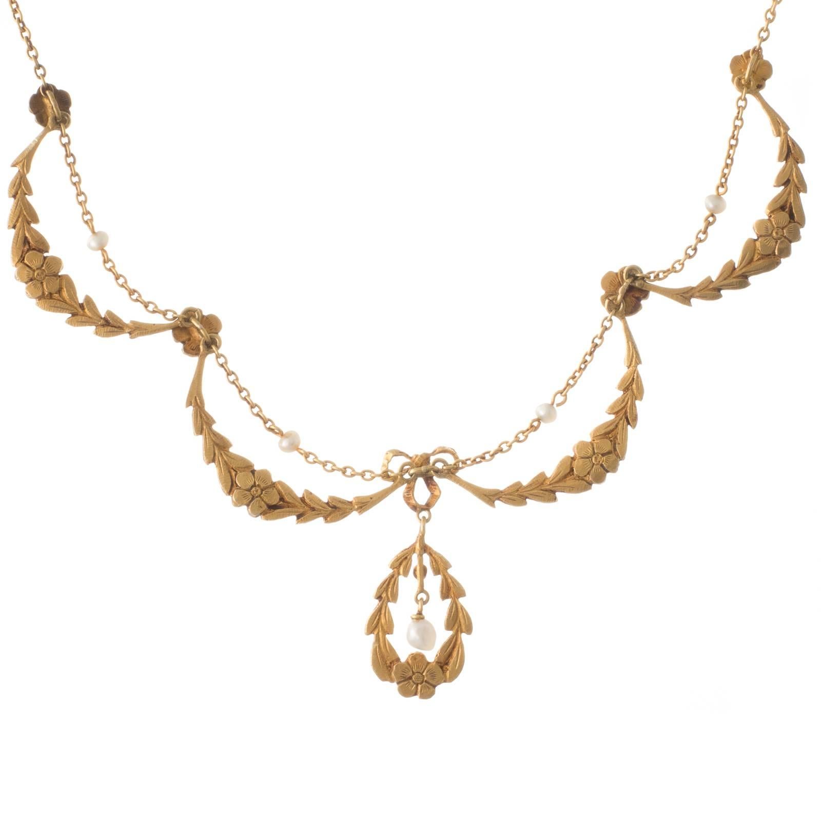 A fine 18ct yellow gold French antique necklet with four garland style swags meeting in the centre with a bow, from which is suspended a floral wreath with a seed pearl to its centre; the garlands are separated by individual flowers and above each a