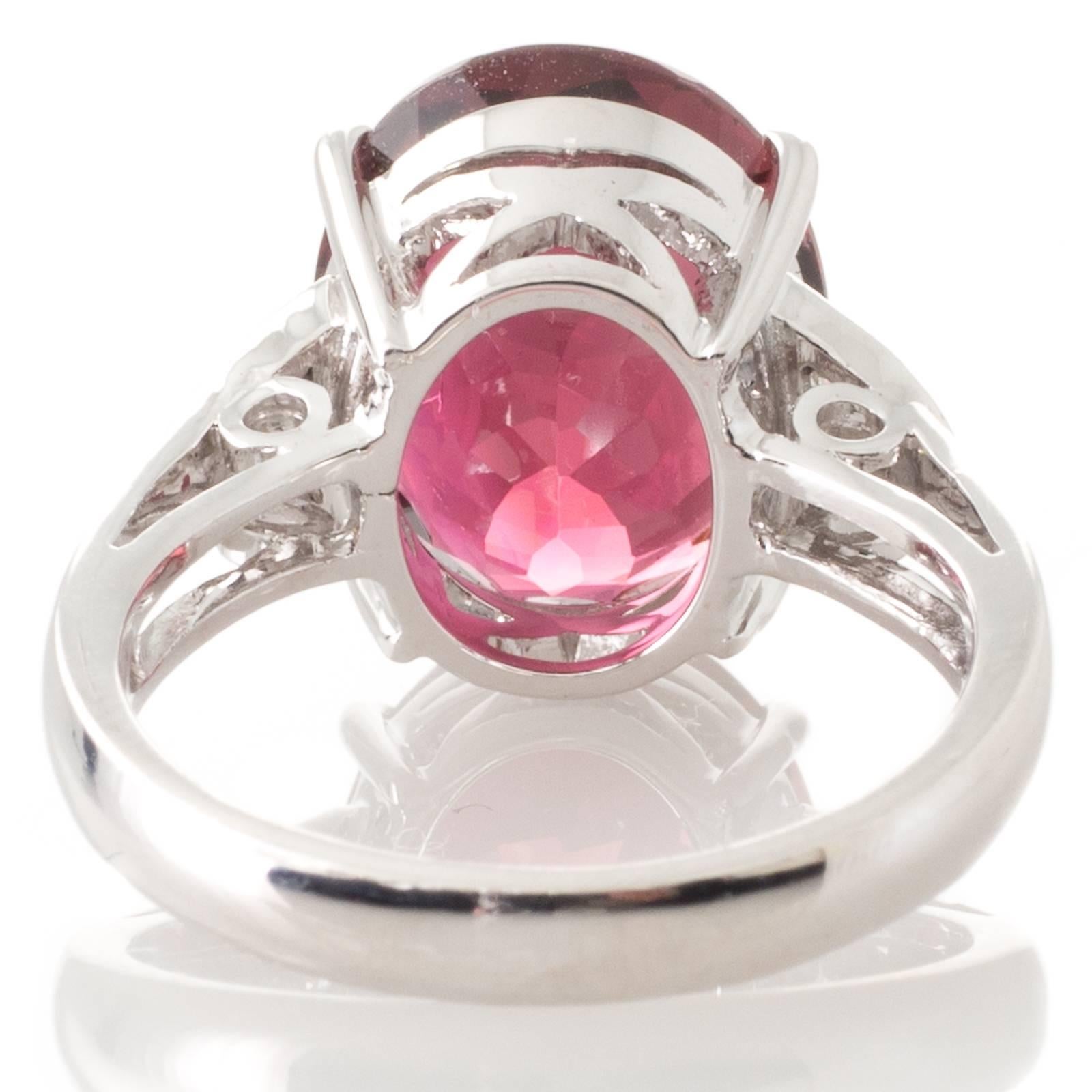 An 18ct white gold ring four claw set to the centre with a 7.03ct oval faceted pink tourmaline above a lattice pierced gallery to upswept shoulders each with a triangular top which is grain set with three diamonds all to a plain polished shank.