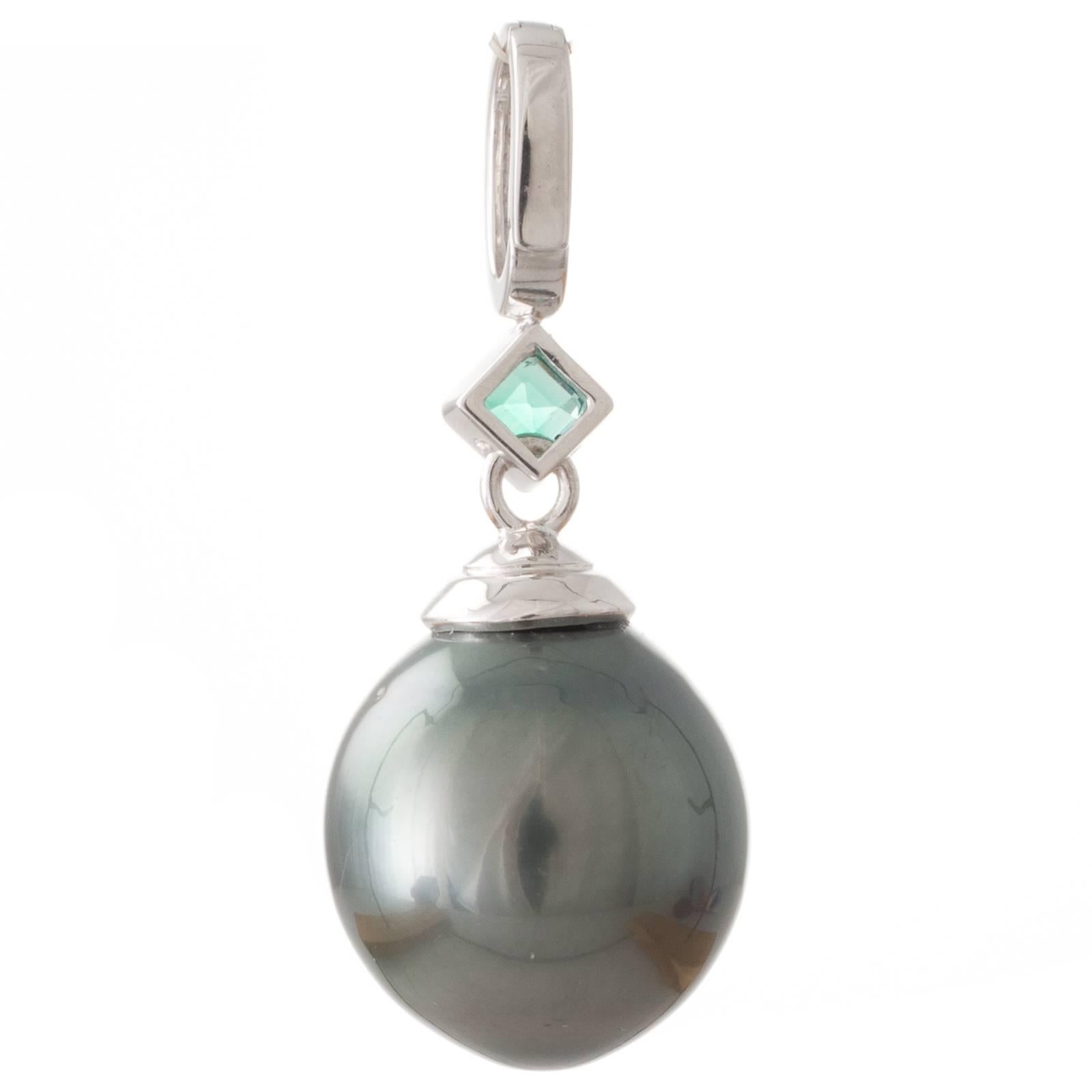A Tahitian pearl 15-16mm oval/drop shape green hue with very good lustre and few natural surface marks near top of the pearl set as an enhancer pendant in 9ct white gold with diamond set clip atop a bezel set 0.25ct emerald cut emerald angled onto