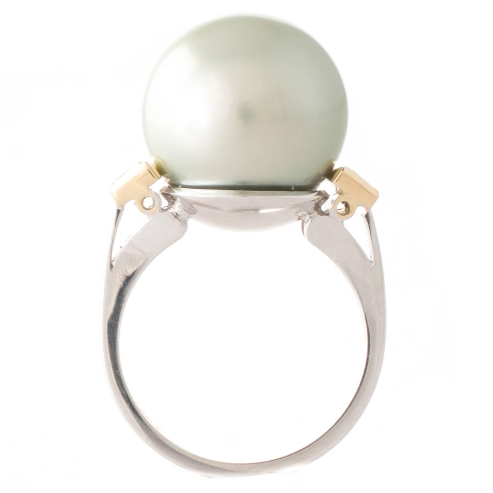 A Tahitian pearl ring featuring a 14.9mm round dark silver/grey green hue (pistachio coloured) Tahitian South Sea pearl with high lustre and very few natural surface marks set into a ring of 18ct white gold with a pair of trapezoid shape fancy