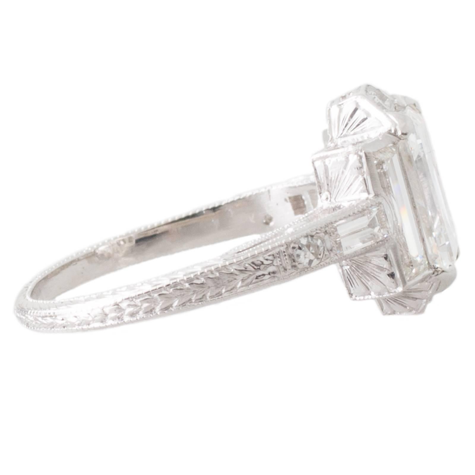 Platinum Art Deco ring set in four corner claws to the centre with a GIA certified 1.38ct rectangular step cut diamond graded as colour G clarity VS1 flanked to either side with a baguette cut diamond and grain set to the top and bottom ends with
