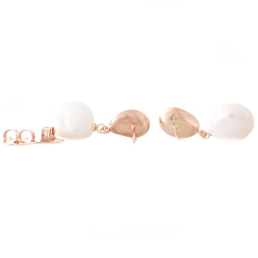 A pair of rose gold plated drop stud earrings featuring pebble shaped white Freshwater pearls measuring 13mm articulated from matte finish pebble shaped gold plated studs.