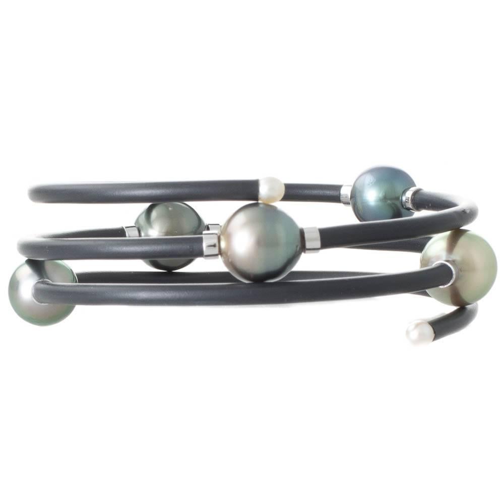 A black neoprene steel coil bangle featuring five scattered semi-baroque shaded green Tahitian pearls measuring 9 - 10mm with a good lustre and few natural surface marks. Each pearl is supported by 9ct white gold connectors.