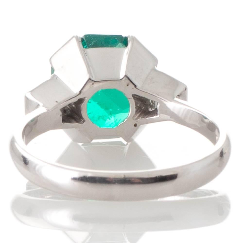A handmade 18ct white gold ring featuring a 2.94ct octagonal cut emerald accompanied by a CDC Gemstone Report stating origin as Colombian set within four wide claws between a pair of trapezoid cut diamonds in bezel settings diamonds of total weight