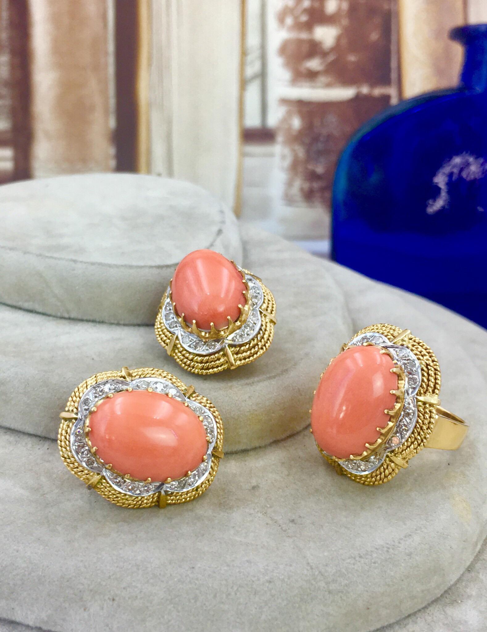 A set of coral and diamond jewellery. The ring designed as an oval coral cabochon with single-cut diamond and rope-twist scalloped surrounds, together with matching earrings. Estimated total diamond weight 0.70ct. Length of earrings 2.4cms. Weight